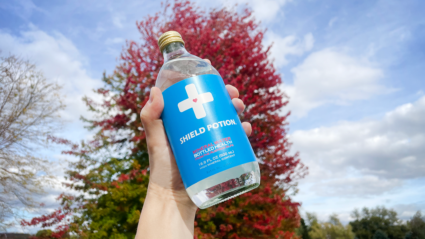 hand holding Shield Potion bottle up in the air showing a beautiful fall tree and landscape in the background